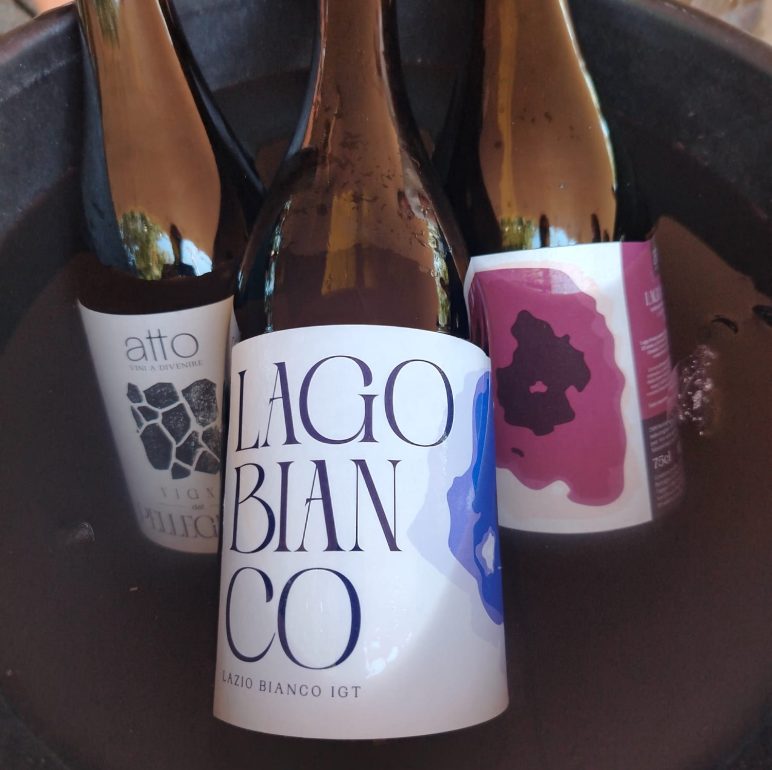 Wine bottles chilling in a black ice bucket, labels visible including Lazio Bianco IGT at the center bottle.